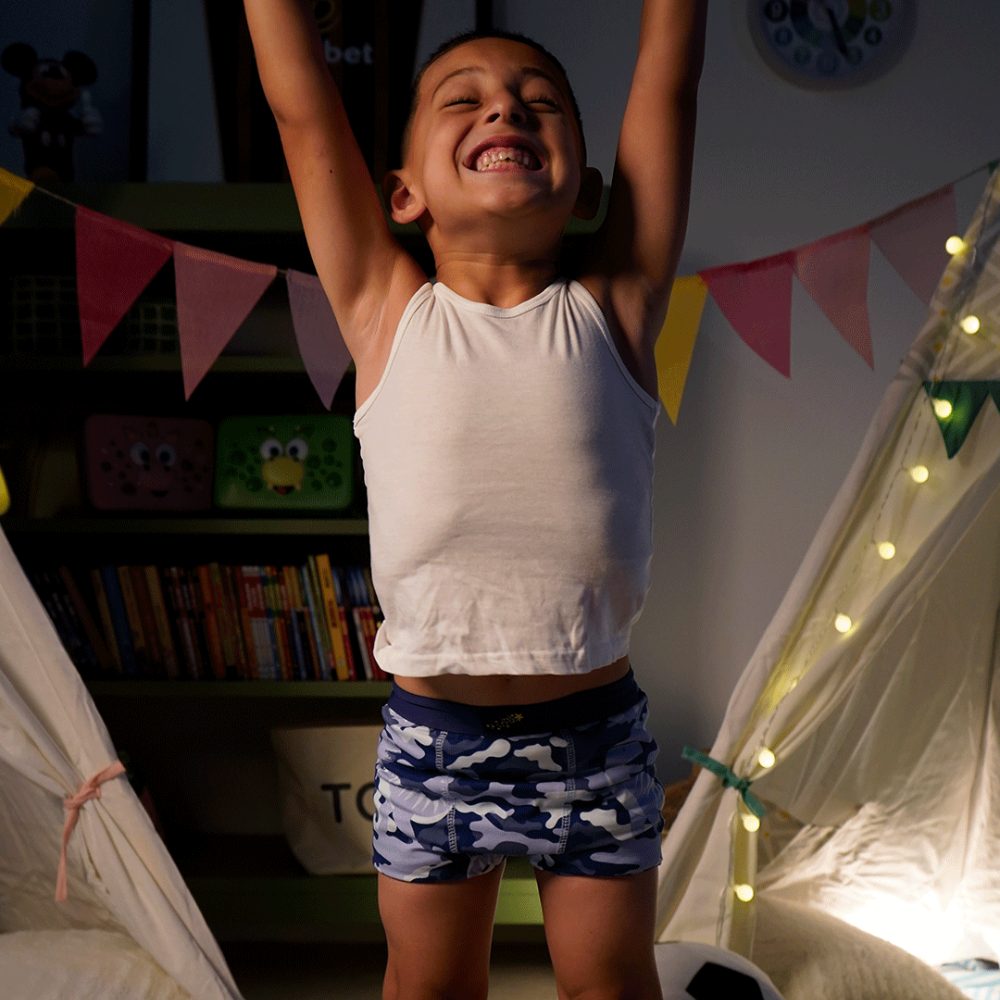 A boy jumping in the air in a bedroom wearing blue My Magic Nighttime Pants by My Carry Potty