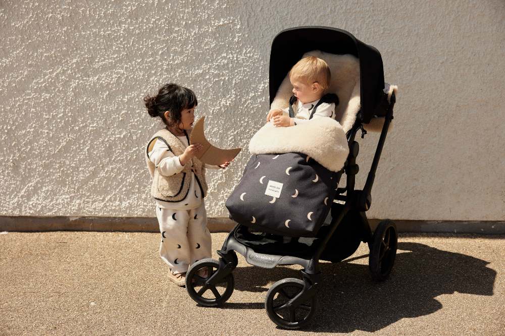 A child stood outside beside a baby in a buggy