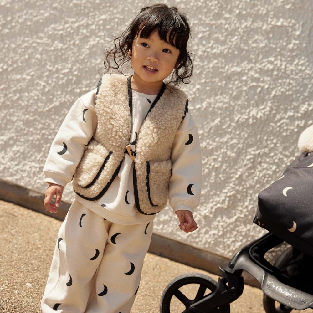 A girl stood outside by a pram wearing a moon print outfit from the Organic Zoo and BINIBAMBA limited edition Midnight collaboration 