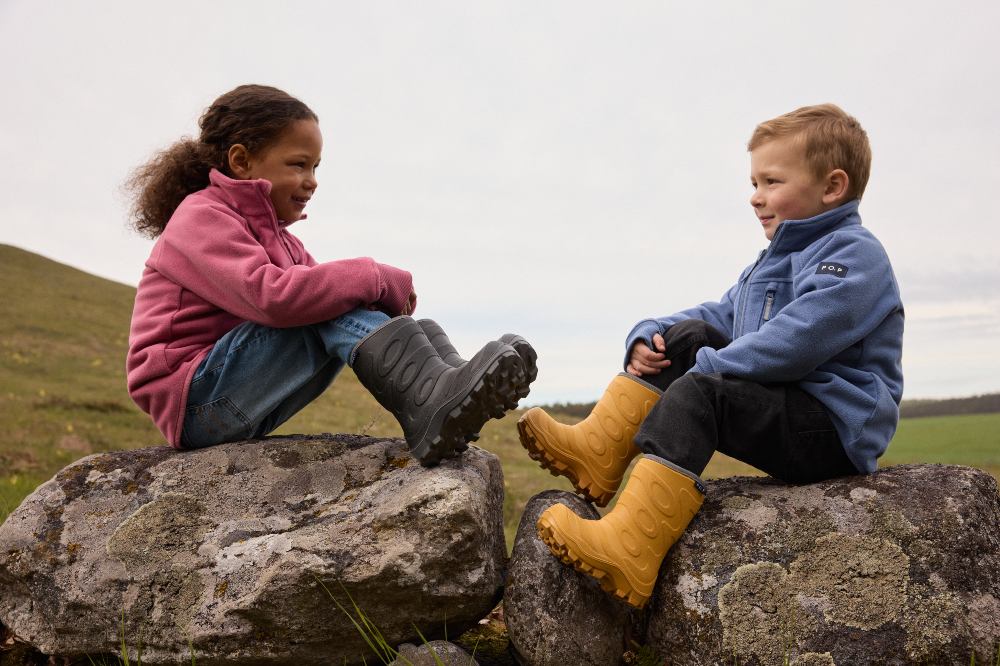 Two children sat outside on a wall wearing wearing wellingtons and outwear by PO.P