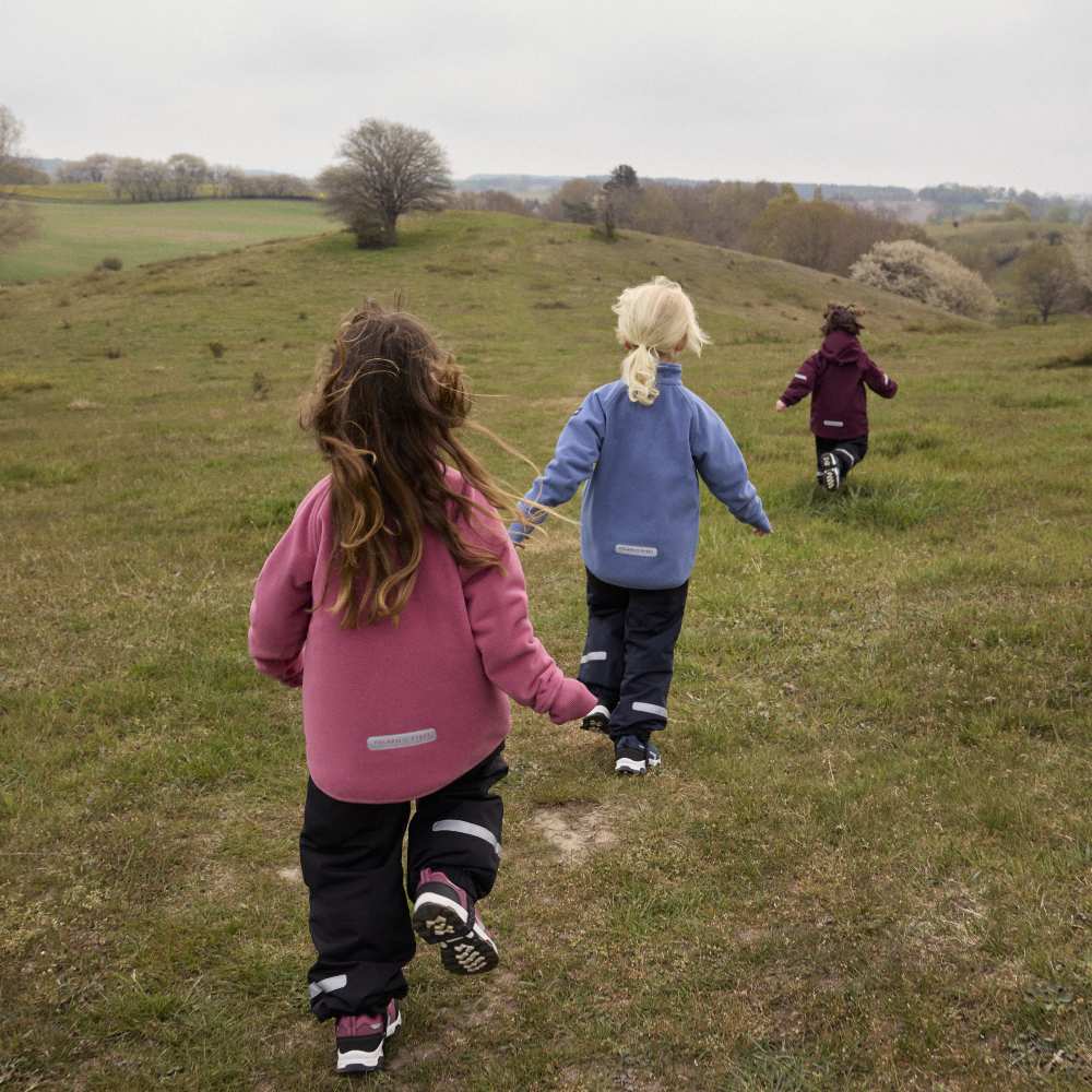 Three children running outside in a field wearing outerwear by PO.P