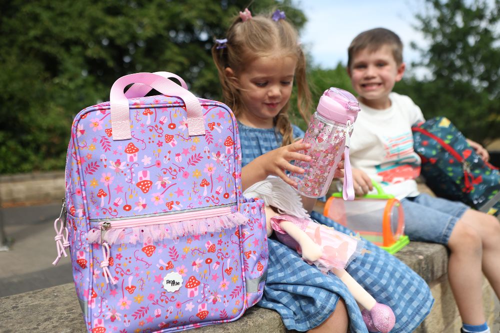Two children sat on a wall with rucksacks and waterbottles by Roamie