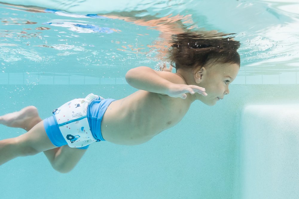 A baby swimming in a pool wearing the new YULEX® Happy Nappy Hero swim nappy