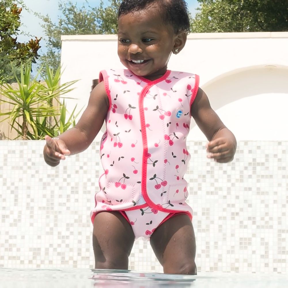 A girl in a pool wearing a cherry print swim vest and bottoms by Splash About 
