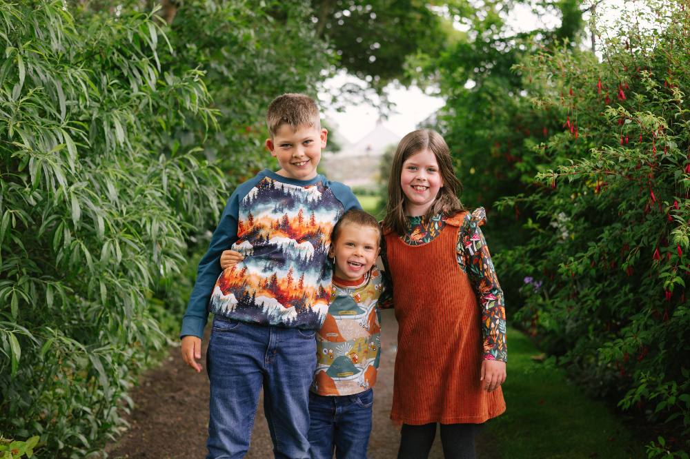 Three children stood outside wearing colourful outfits by Boannie Riggit