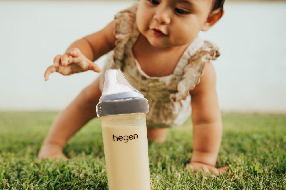 A baby crawling on grass towards a baby bottle by Hegen