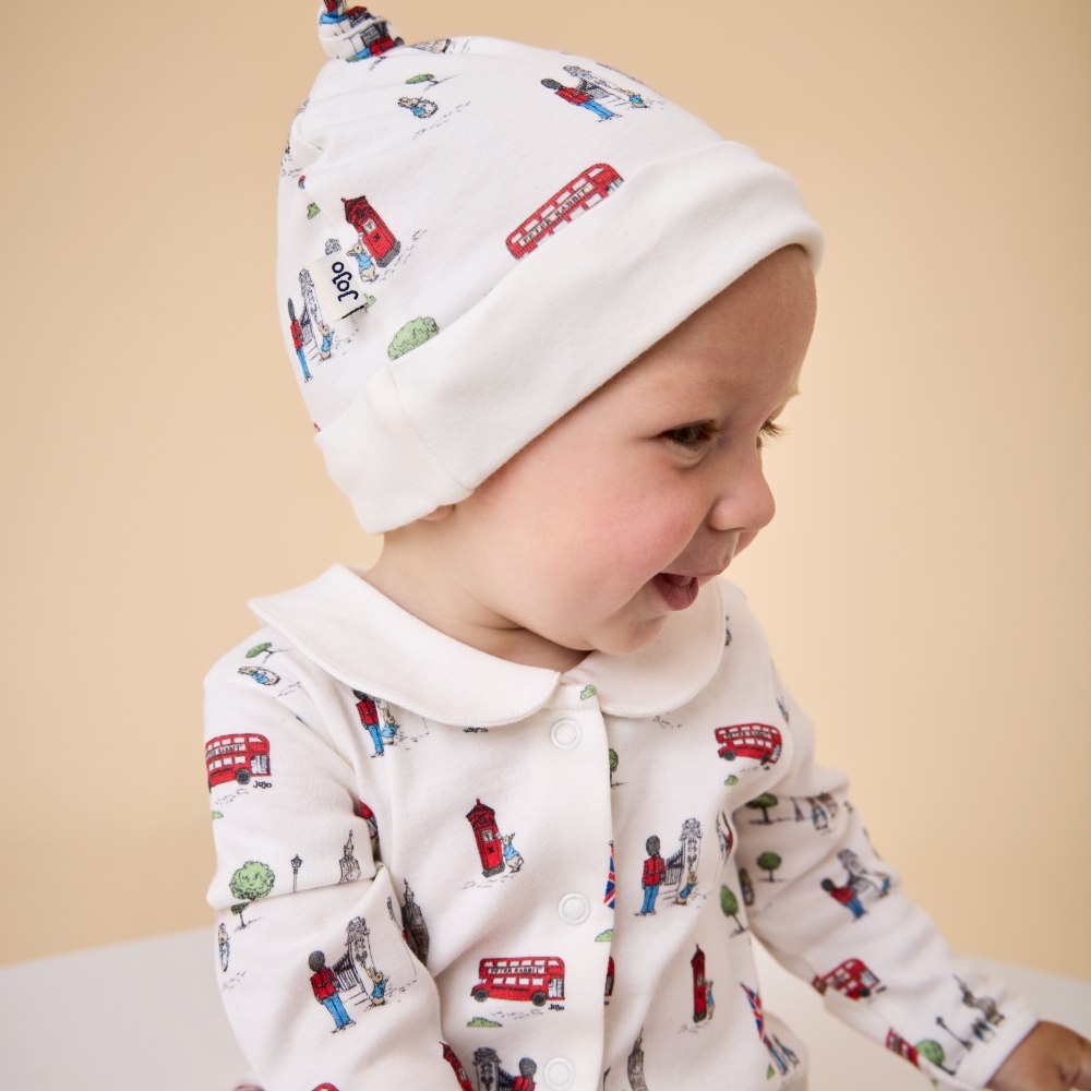 A baby in a Peter Rabbit print hat and babygro by JoJo Maman Bebe
