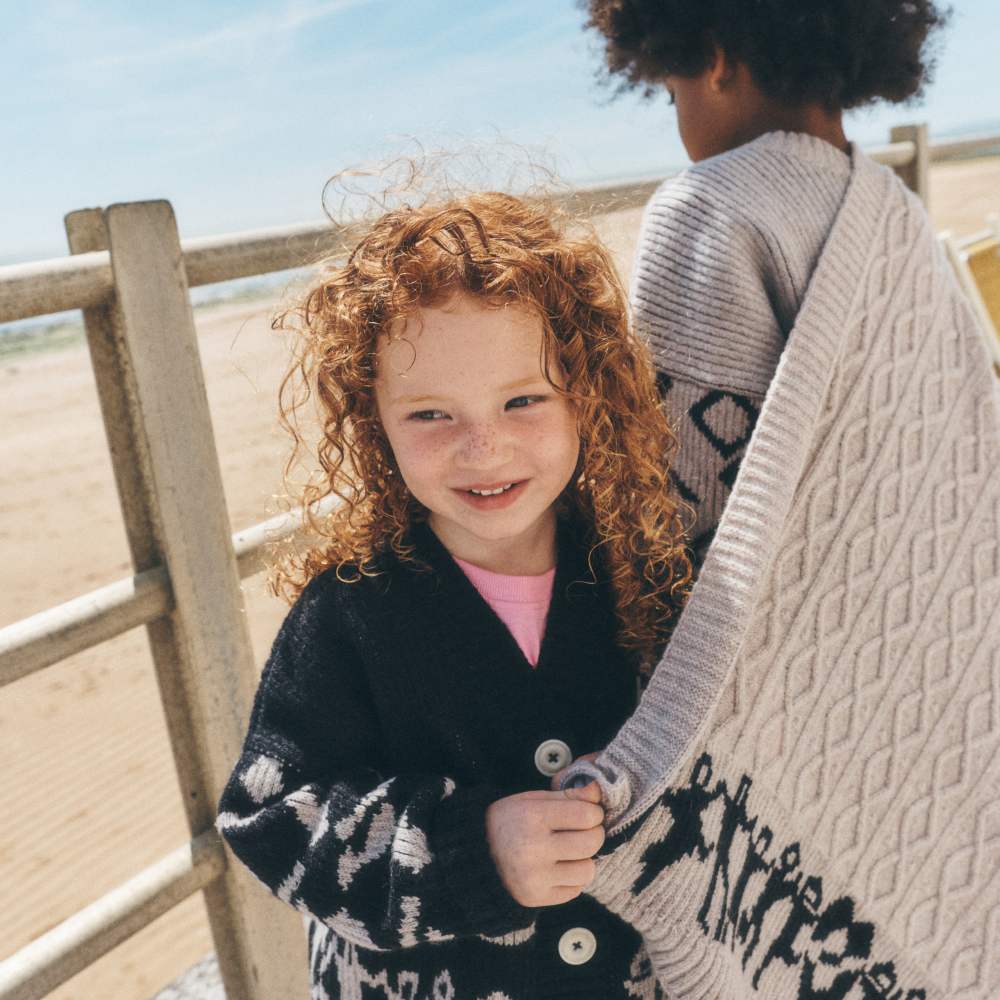 Two children in Talou knitwear on a beach 
