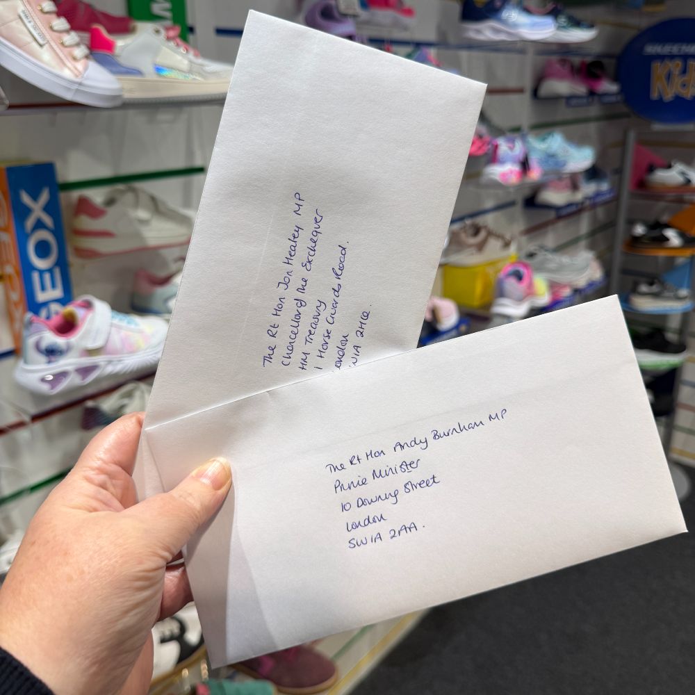 A hand showing holding two letters from The Footwear Hub with a children's shoe shop in the background 